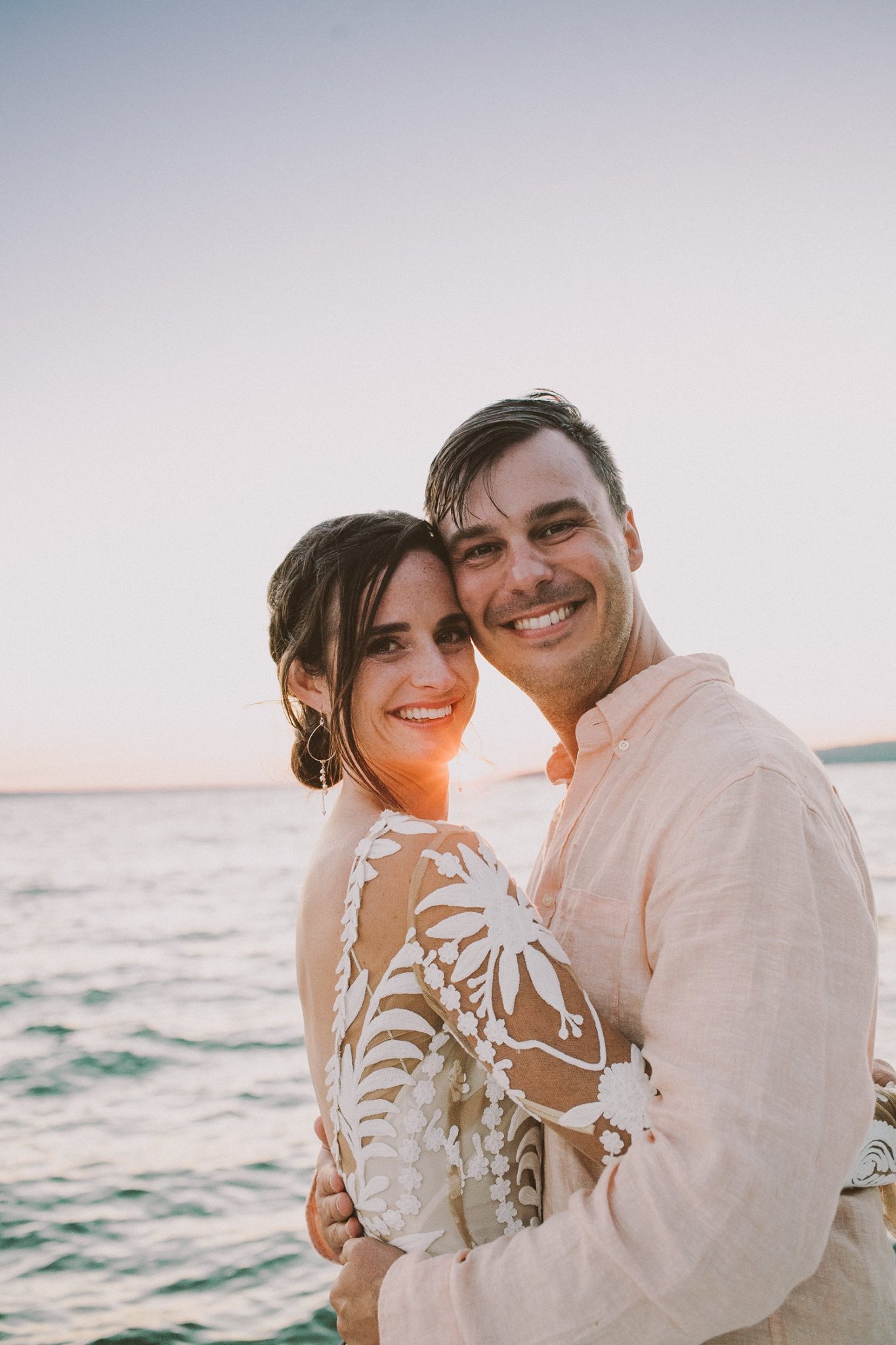 bride and groom embracing next to lake Charlevoix at sunset